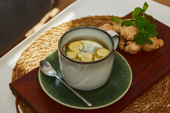 Ein warm servierter Ingwertee mit Zitronenscheiben auf einem Holztablett, begleitet von Ingwerstücken und Minze als wohltuendes Getränk bei Erkältungen.