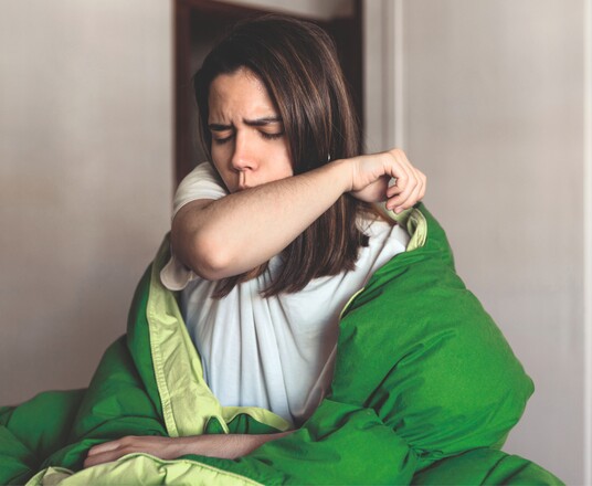 Ansteckung bei Bronchitis: Frau mit Bronchitis hustet.