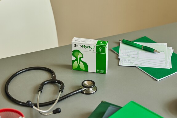 Gelomyrtol Forte – Unverzichtbar für die Gesundheitspflege, abgebildet mit medizinischen Instrumenten und Medikamenten für die Behandlung von Erkältungssymptomen. Auf einem Schreibtisch liegt eine geöffnete Packung Gelomyrtol Forte neben medizinischen Utensilien, darunter ein Stethoskop und ein Notizblock.