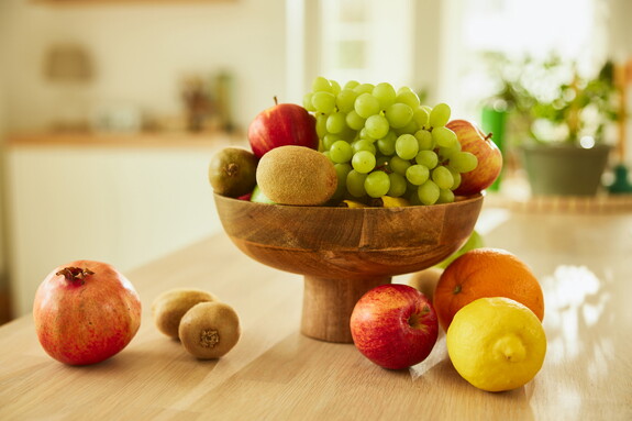Eine Schale mit einer Auswahl an frischen Früchten, darunter Trauben, Äpfel und Zitronen auf einer Küchenarbeitsplatte als Beitrag zu einer gesunden Ernährung und Unterstützung des Immunsystems.