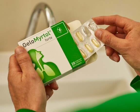 Gelomyrtol forte – Natürliche Hilfe bei Erkältungen, für freie Atemwege und Wohlbefinden. Hände halten eine Packung Gelomyrtol forte und eine Blisterpackung mit Kapseln, bereit zur Einnahme für die Linderung von Erkältungssymptomen.