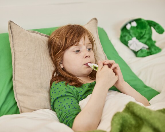 Sinusitis bei Kindern: Fieber messen Kind mit Nasennebenhöhlenentzündung liegt mit Fieberthermometer im Mund im Bett.