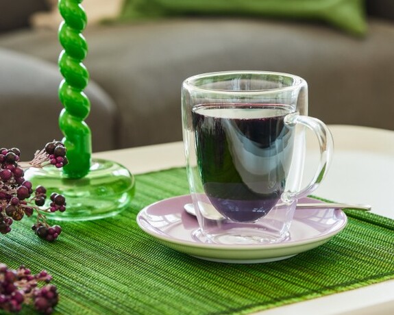Transparente Tasse mit Holunderbeersaft steht auf einem grünen Tischset zur natürlichen Unterstützung des Immunsystems.