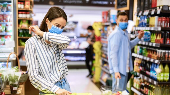 Corona oder Erkältung? Frau mit Maske hustet im Supermarkt.